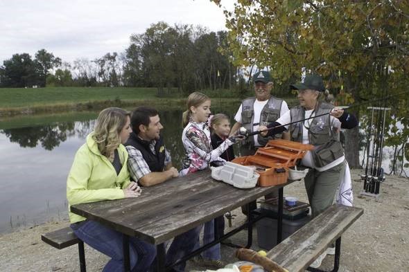 Volunteers teach fishing skills to a family at a picnic table.