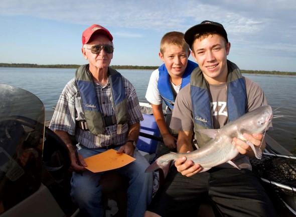 Two brothers and their grandfather pose with a catfish caught on a fishing trip.