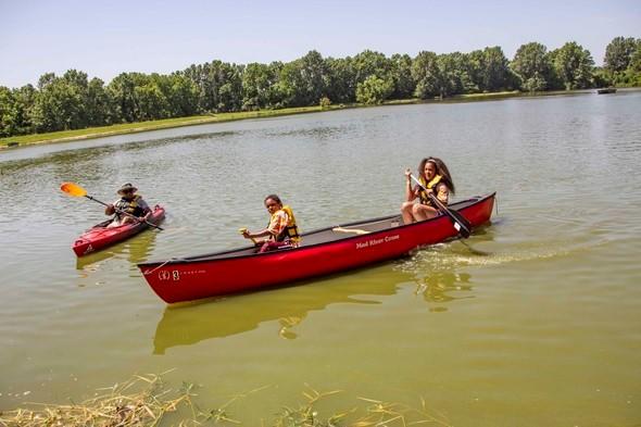 Two girls canoe while another person kayaks