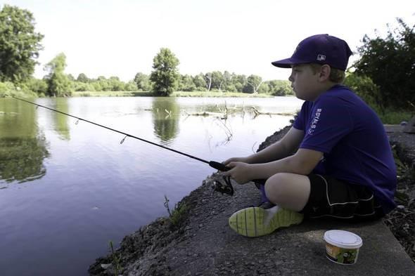 Boy sitting and fishing a pond.
