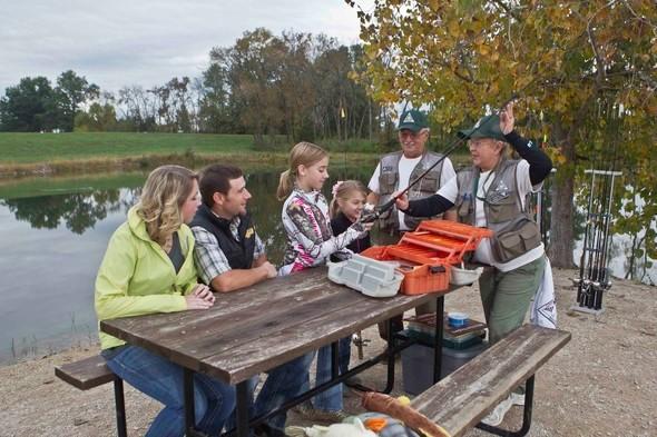 Two conservation agents teach a family the basics of fishing.