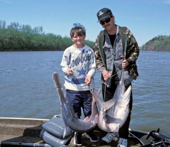 man and boy on boat with two paddlefish