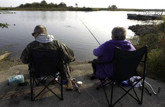 Two people sit in chairs while fishing at a lake
