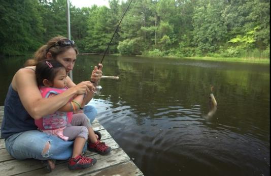 Lady helping a little girl catch a fish.