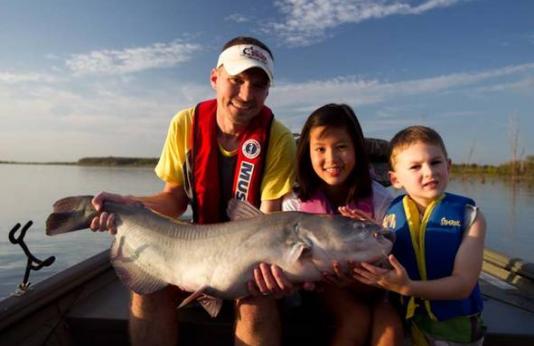 An adult angler and two children hold a large catfish in their boat