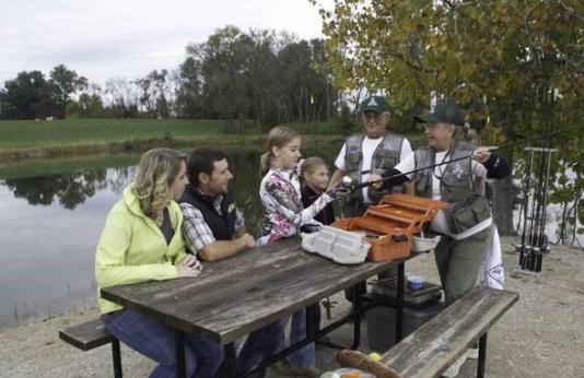 Volunteers teach fishing skills to a family at a picnic table.
