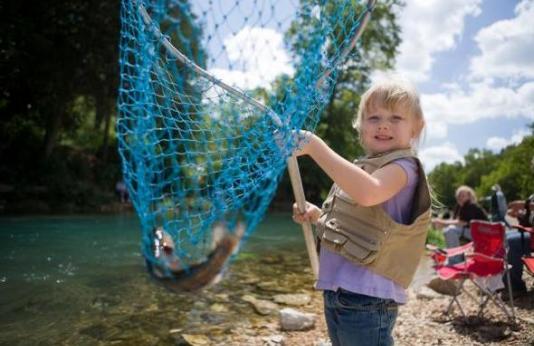 Little girl holding up fish in a net.