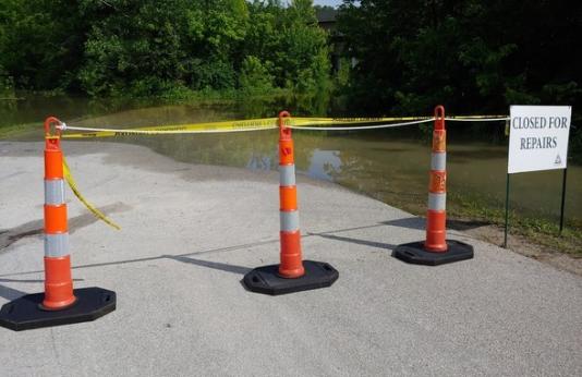 Orange cones and hazard tape across road to conservation area closed from flooding
