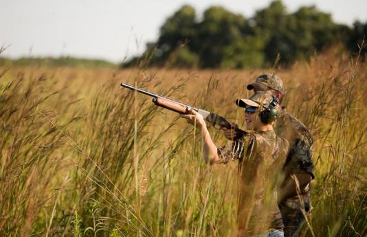 young hunter in field shoots at doves while other hunter watches