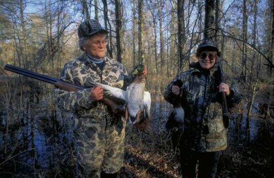 two female duck hunters in woods with harvested ducks in hand